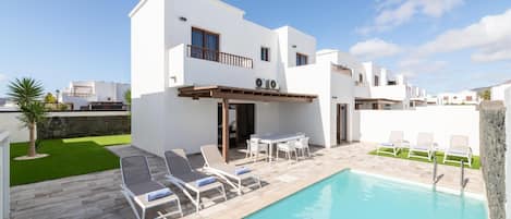 A modern two-story building with a pool, outdoor seating, and a clear sky.