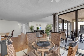 A modern living room with a glass-top dining table surrounded by wicker chairs, a flat-screen TV, and a sofa. - Sea Club #43 - The Shore Thing (Indian Shores)