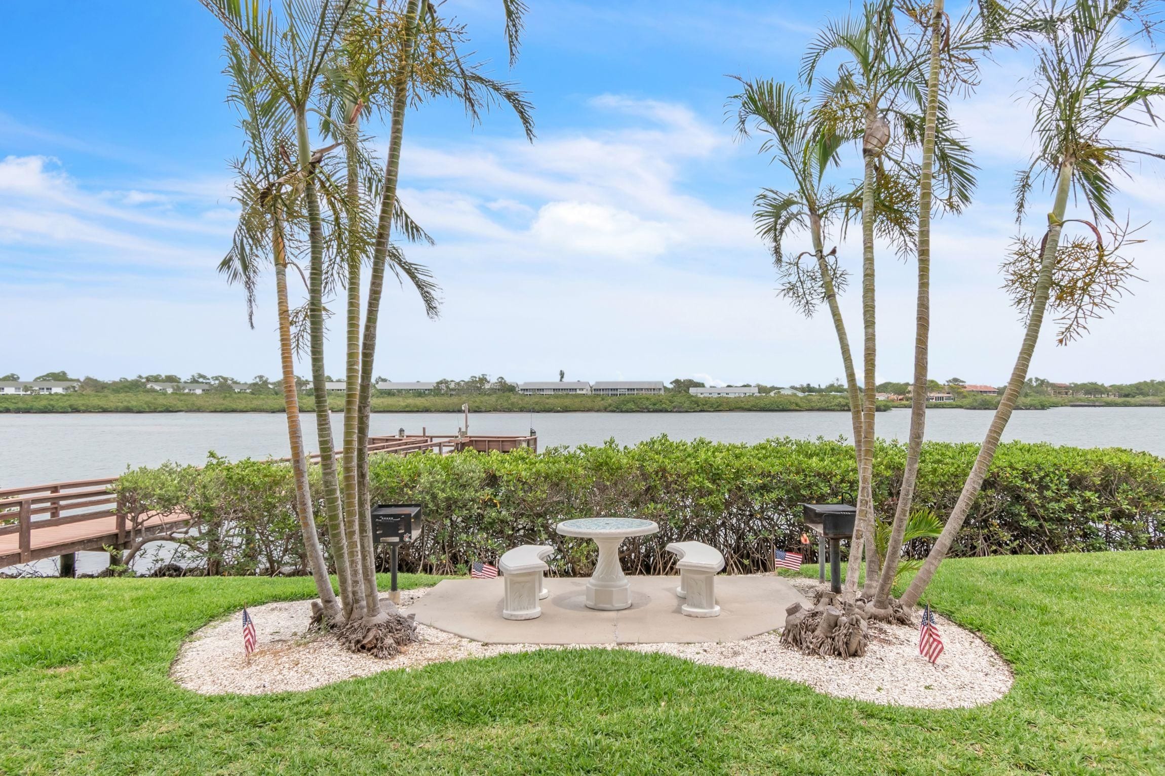 A serene outdoor seating area with a table and benches, surrounded by palm trees and a view of a lake.