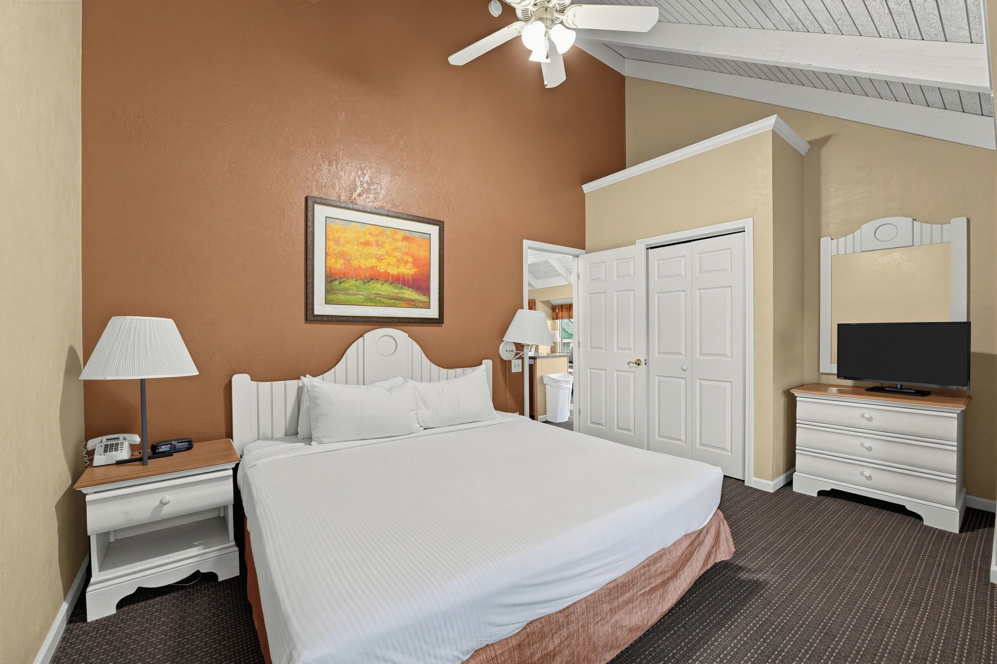 A hotel room with a bed, bedside tables, a lamp, a painting, a television, and a wardrobe.