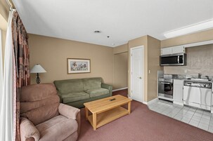 A compact living space with a sofa, a coffee table, a kitchenette, and a door.
