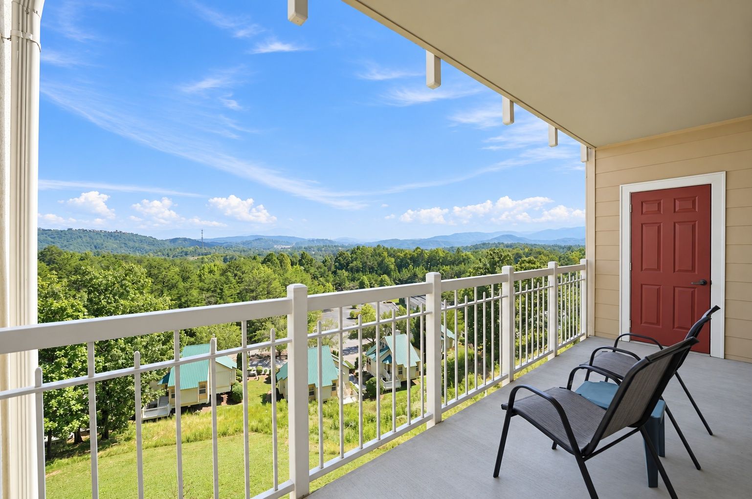 A balcony with a white railing, two chairs, and a red door.
