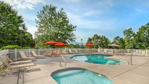 A pool area with two pools, lounge chairs, and red umbrellas. - Sunrise Ridge Resort  (Pigeon Forge)