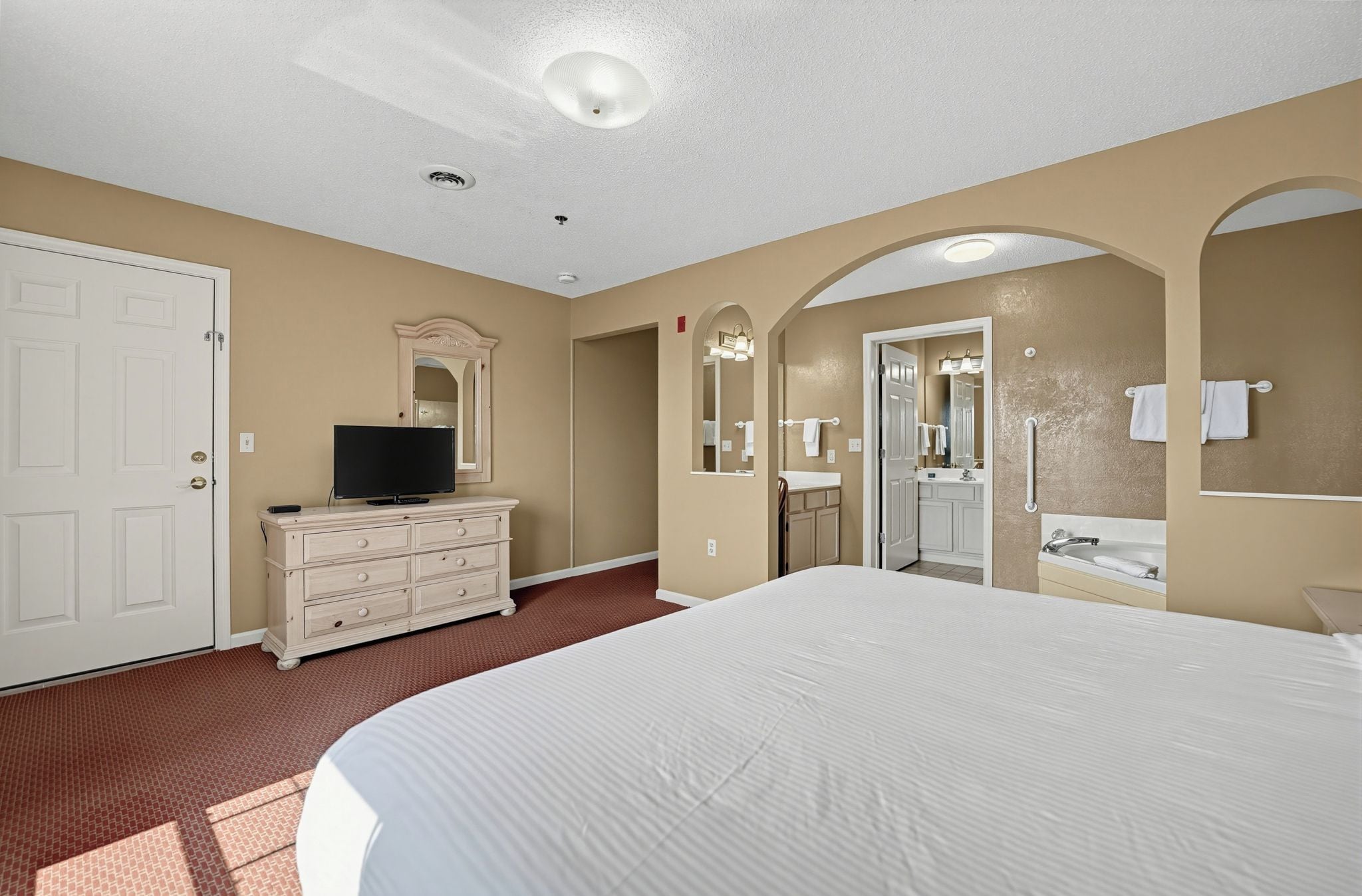 Een hotelkamer met een groot bed, een kapstok, een televisie, een badkamer met spiegel en een deur.