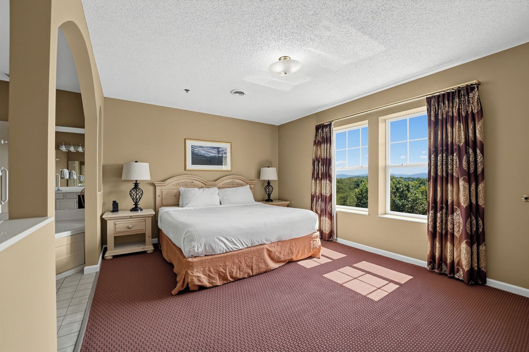 Habitación de hotel con una cama grande, dos lámparas de noche, un ventanal con cortinas y vistas al exterior.
