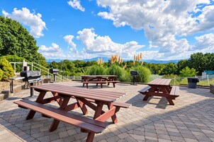 An outdoor patio with picnic tables, a barbecue grill, and a trash can.