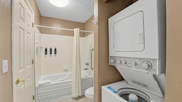 A bathroom with a bathtub, toilet, and a front-loading washing machine.
