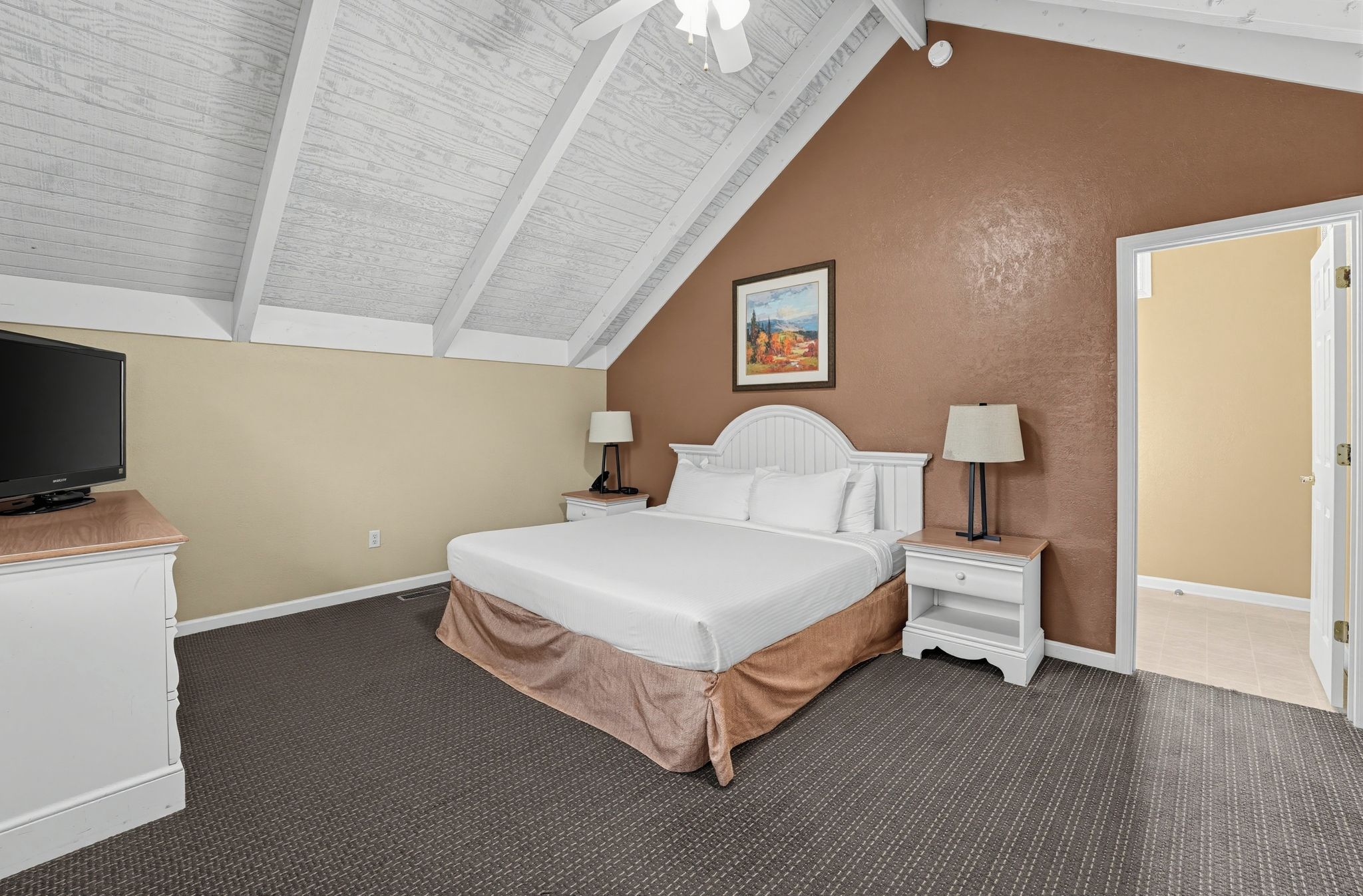 A hotel room with a bed, two bedside tables, a television, and a painting on the wall.