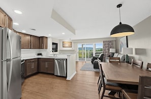 A modern kitchen with stainless steel appliances, a dining area with a wooden table, and a view of a balcony. - Sunrise Ridge Resort  (Pigeon Forge)