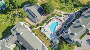 An aerial view of a residential area with a swimming pool surrounded by a deck, a covered patio, and a small garden area.