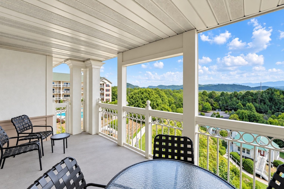 A balcony with a clear view of a mountainous landscape, furnished with chairs and a table.