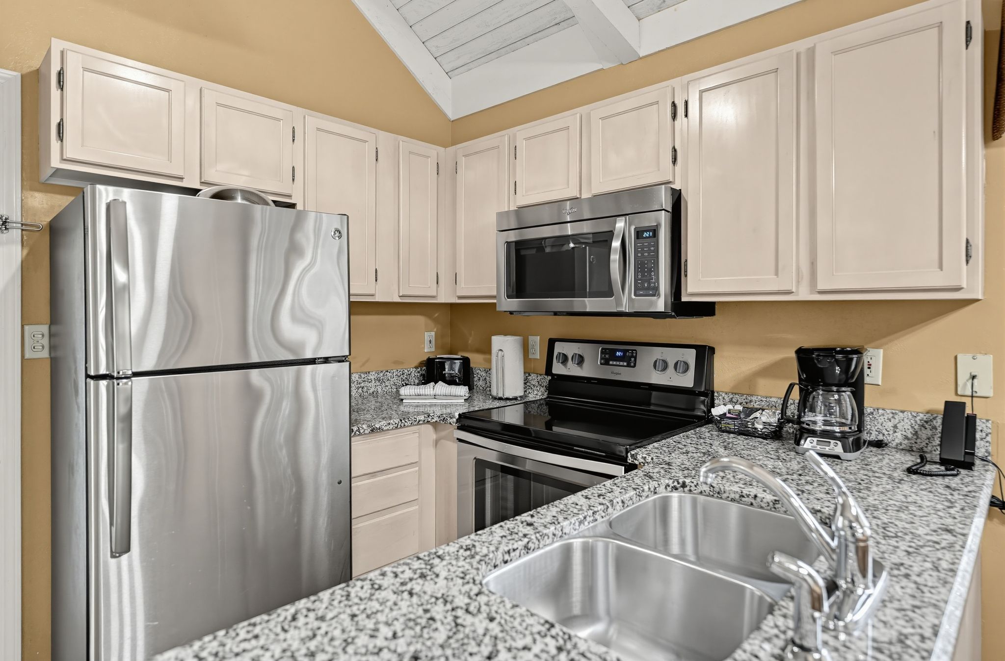 Una cocina moderna con electrodomésticos de acero inoxidable, encimeras de granito y armarios color beige.