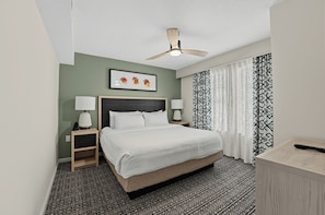 A hotel room with a bed, two bedside tables, a ceiling fan, a framed artwork, patterned curtains, and a patterned carpet. - Sunrise Ridge Resort  (Pigeon Forge)