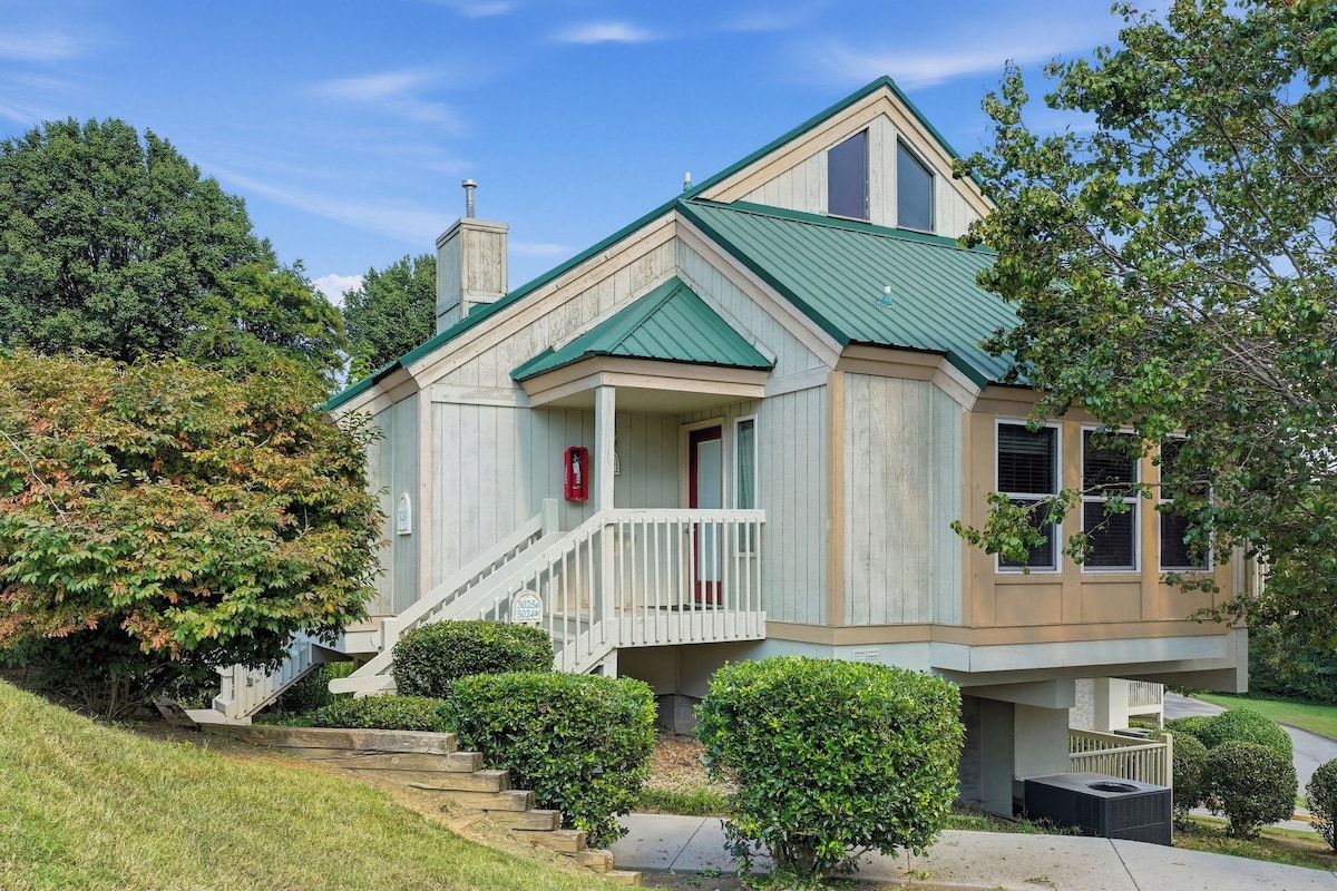 A two-story house with a green roof, a front porch, and a staircase leading to the entrance.