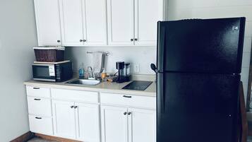 A kitchen with white cabinets, a black refrigerator, a microwave, a sink, and a patterned rug.