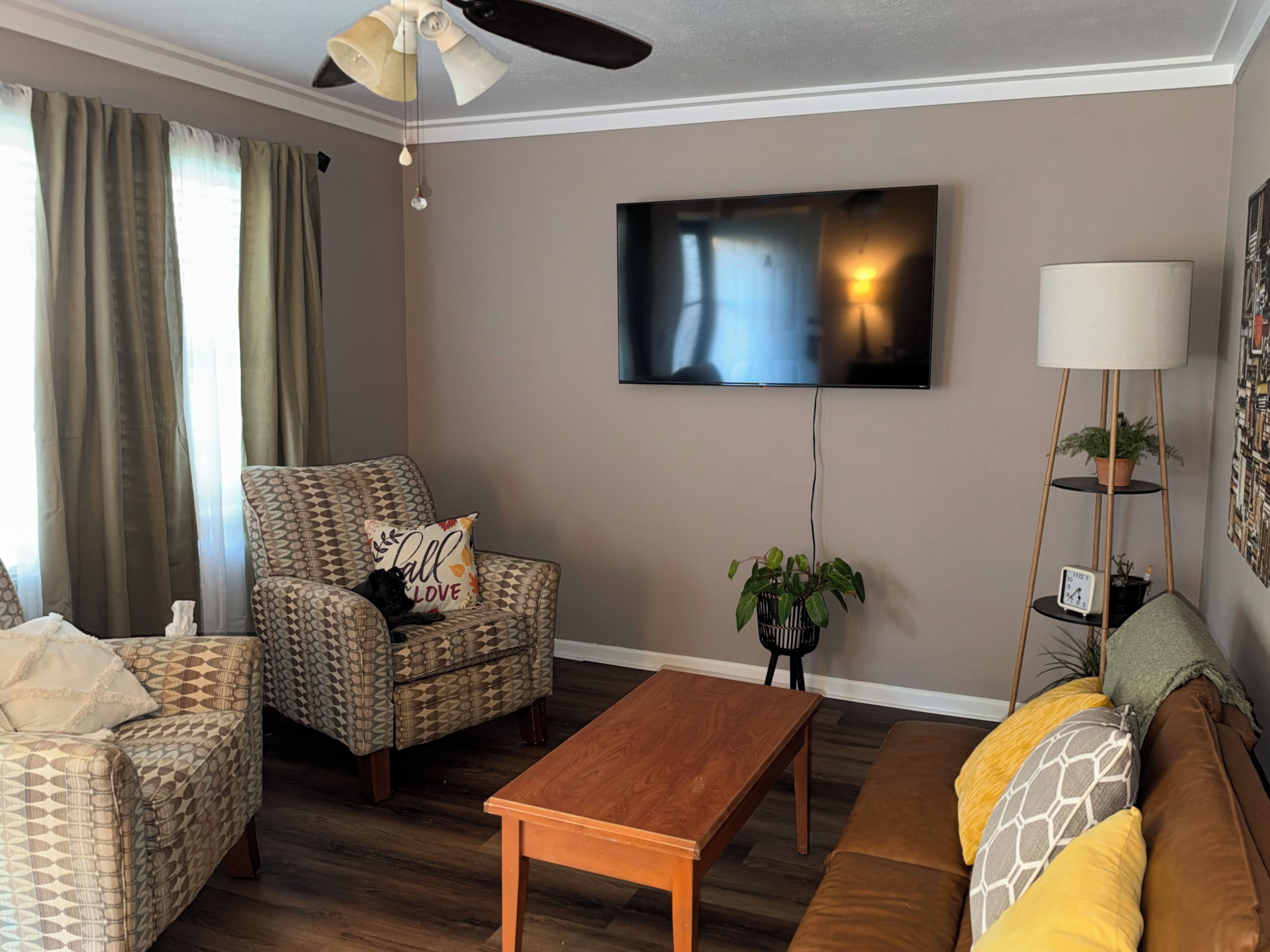 Una sala de estar con sofá, sillón, mesa de centro y televisor montado en la pared.