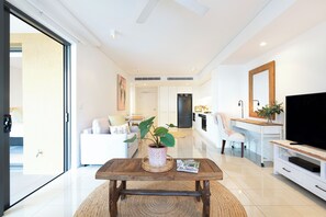 A modern living room with a wooden coffee table, a television, and a dining area with a white sofa and chairs. - The Salty Lagoon A Vibrant Retreat by the Water (Darwin)