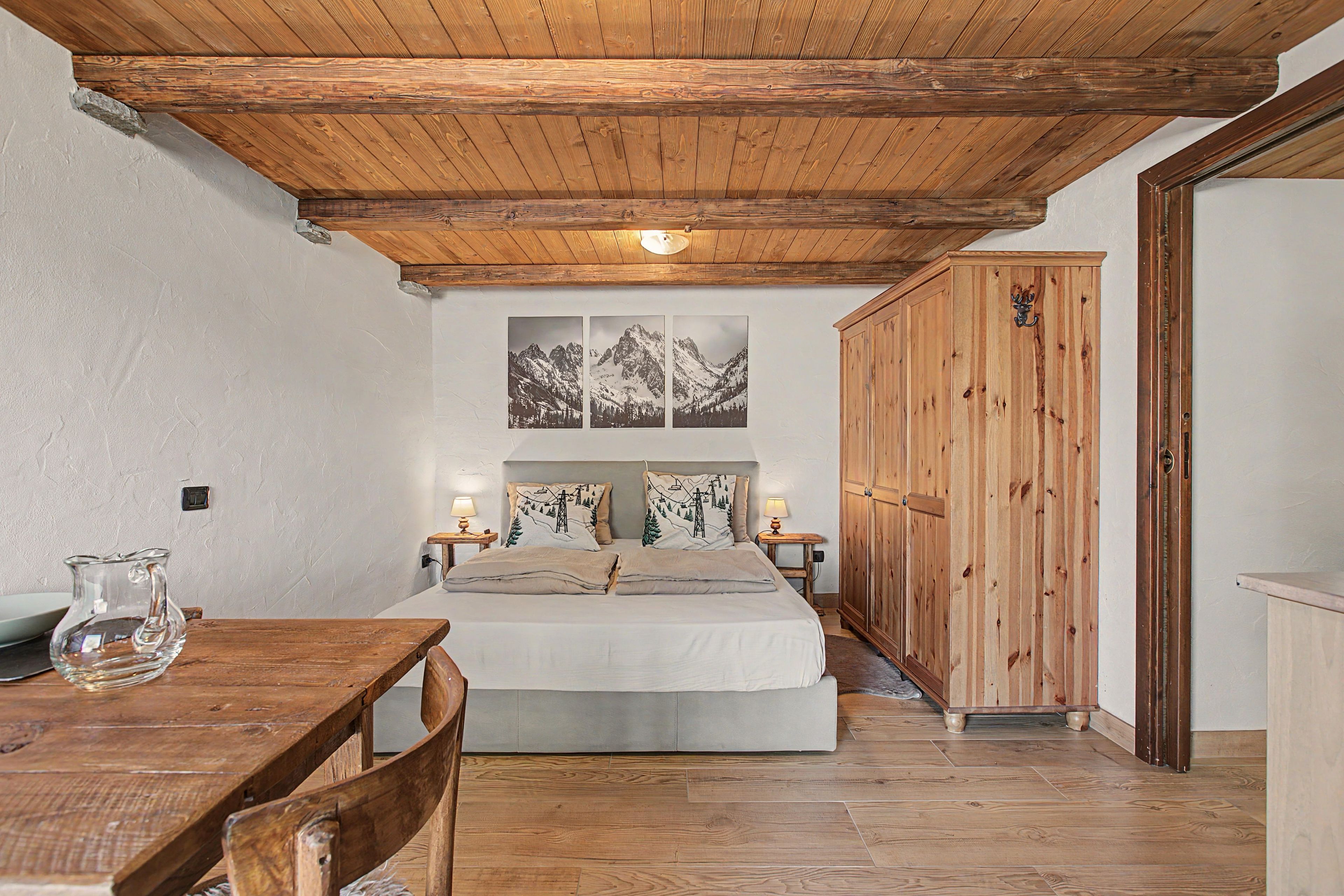 Un dormitorio con techo de madera, una cama con cabecera de temática de montaña, un armario de madera y una mesa con sillas.