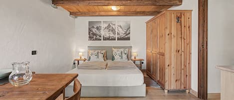 A bedroom with a wooden ceiling, a bed with a mountain-themed headboard, a wooden wardrobe, and a table with chairs.
