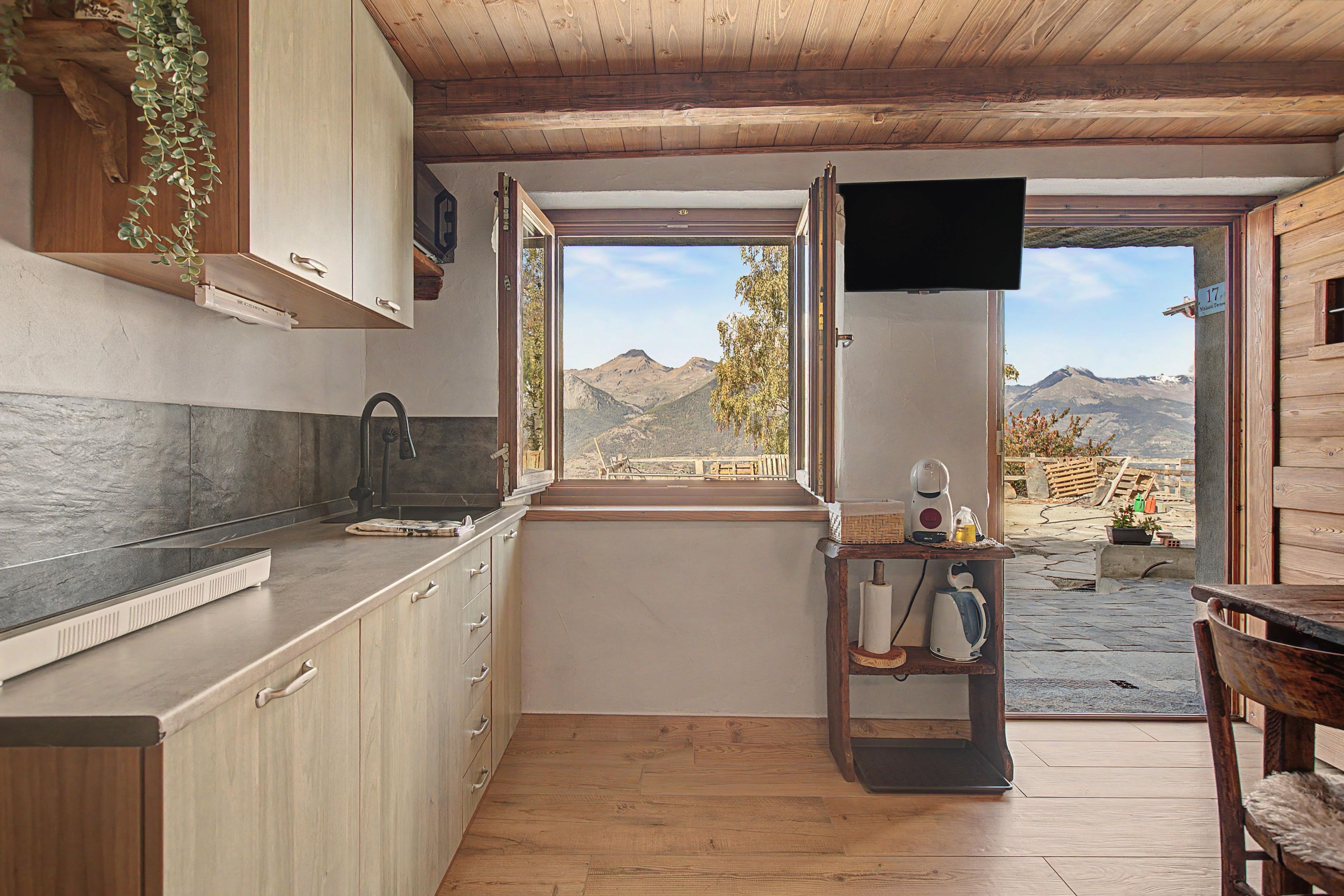 A kitchen with wooden cabinets, a countertop, a sink, and a window overlooking a mountainous landscape.