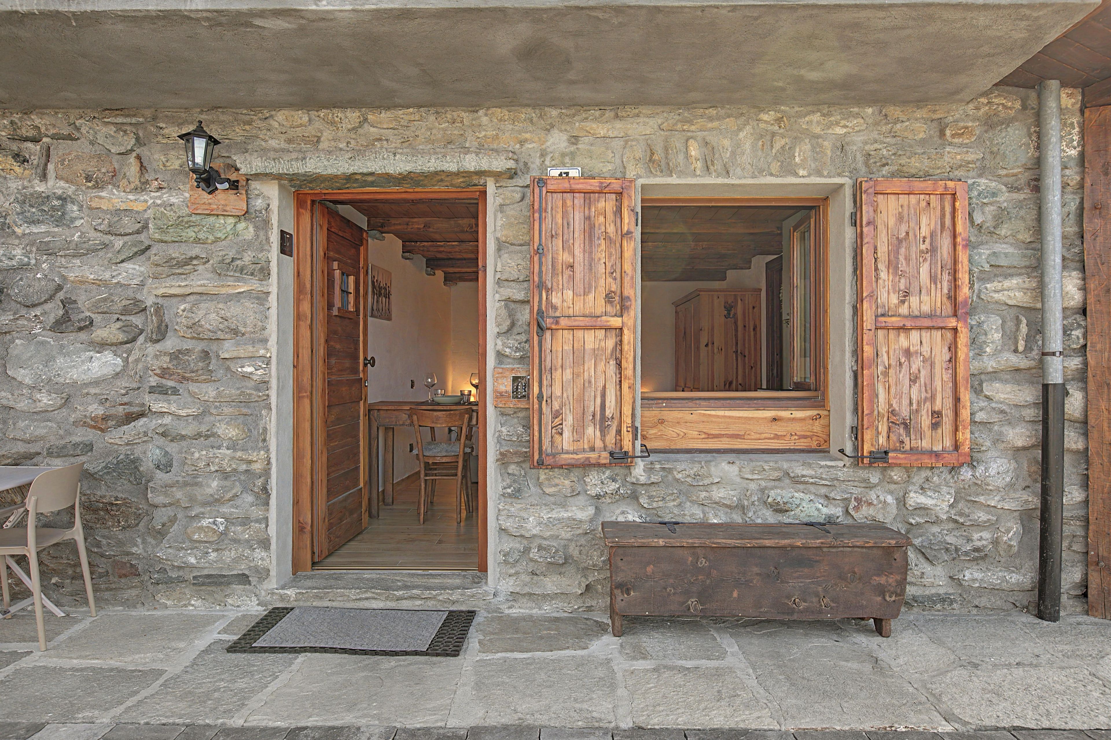 A stone building with wooden shutters, a bench, and a door leading inside.
