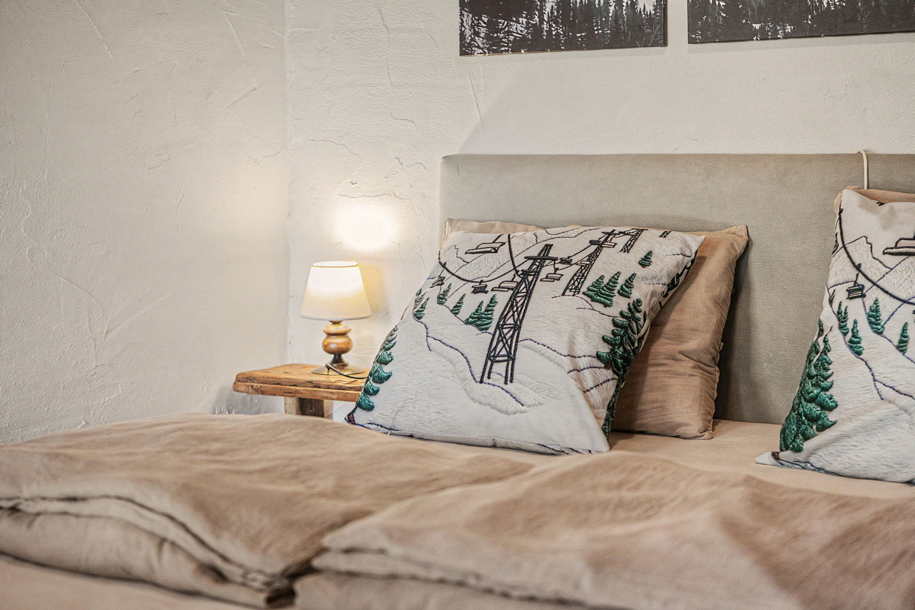 A bedroom with a bed, pillows, a nightstand, a lamp, and a wall with framed pictures.