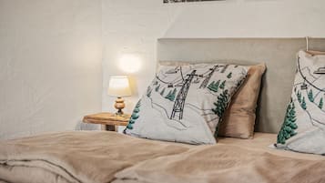 A bedroom with a bed, pillows, a nightstand, a lamp, and a wall with framed pictures.