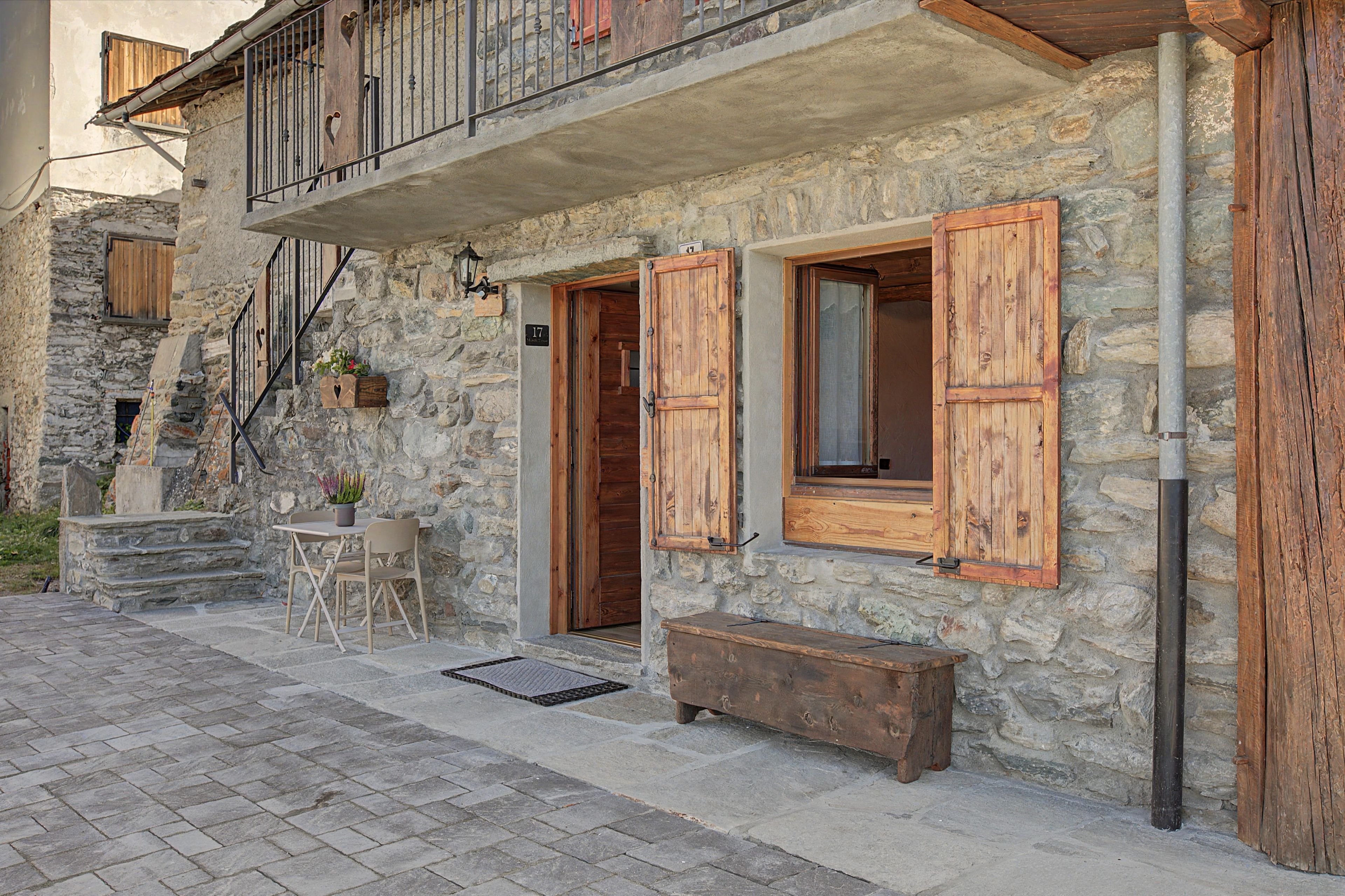 A stone building with wooden shutters, a balcony, and a small outdoor seating area.