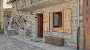 A stone building with wooden shutters, a balcony, and a small outdoor seating area.