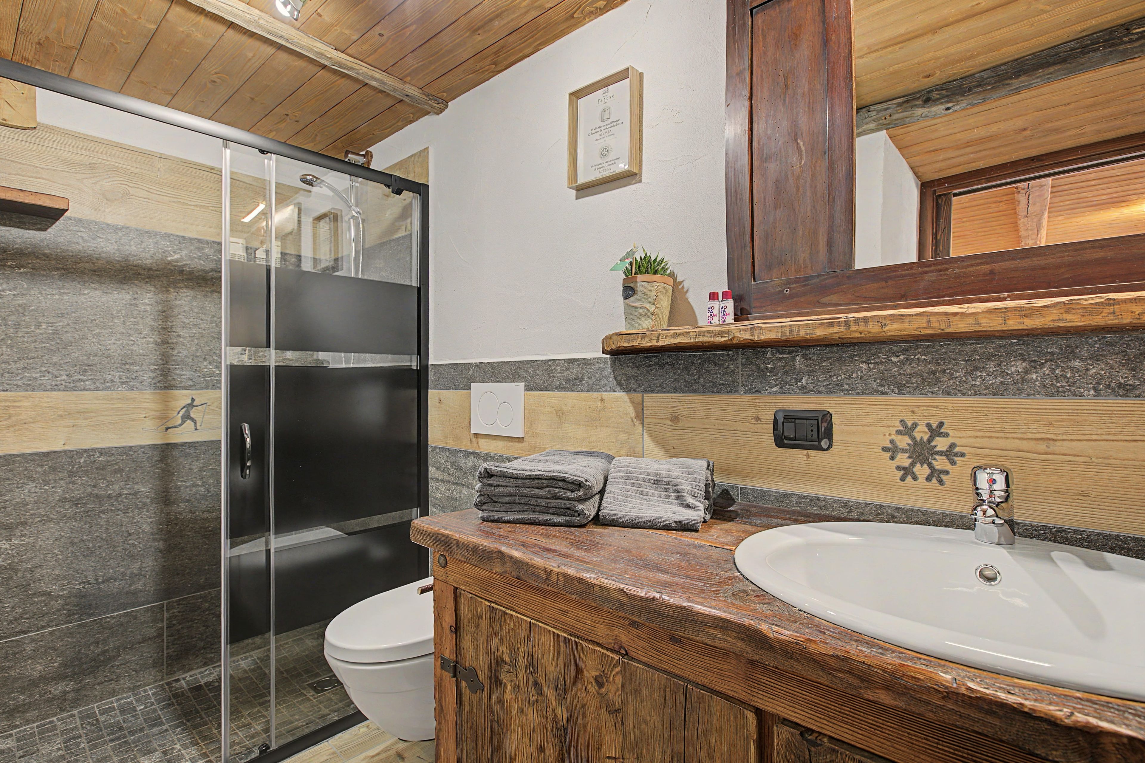 A bathroom with a glass shower enclosure, a white toilet, a wooden vanity with a sink, and a mirror above the vanity.
