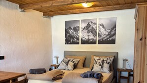 A bedroom with a wooden ceiling, a bed with multiple pillows, a table, and a chair.