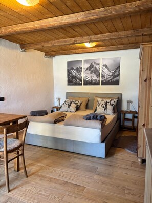 A bedroom with a wooden ceiling, a bed with multiple pillows, a table, and a chair.