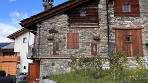 A stone building with wooden shutters, a balcony, and a small garden area.