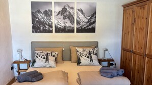 A cozy room with a bed, wooden furniture, and mountain landscape artwork.