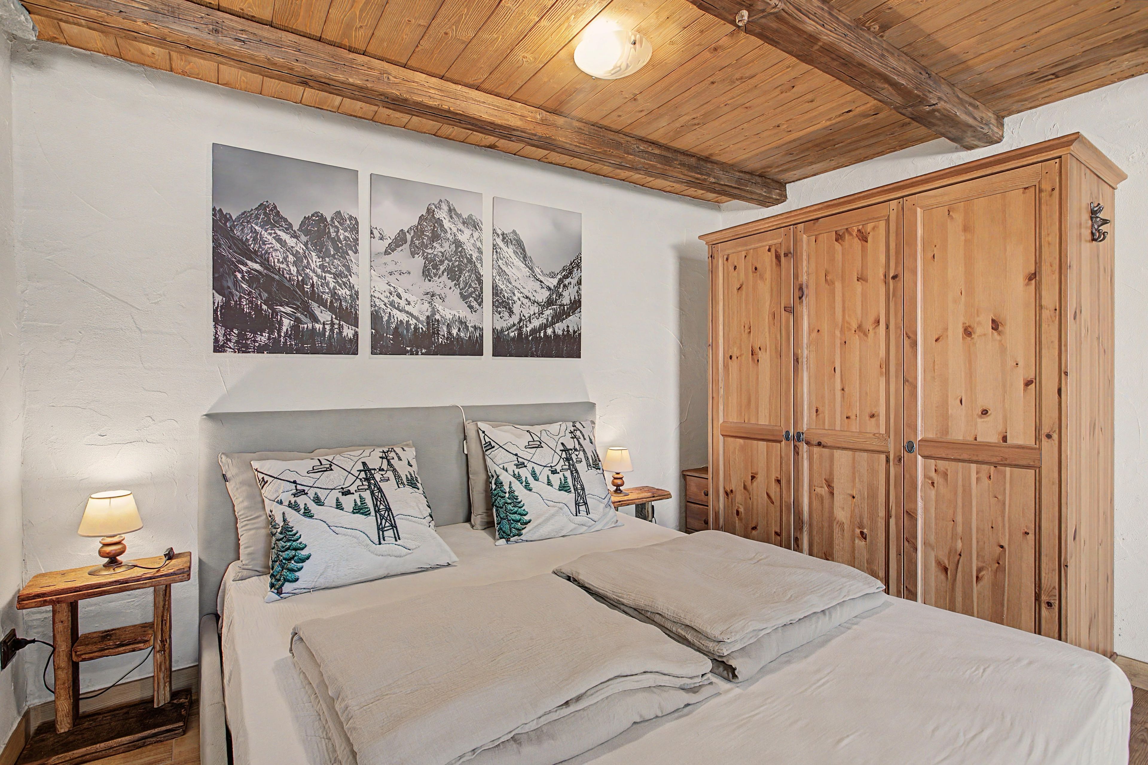 A bedroom with a bed, two nightstands, a wooden wardrobe, and three framed pictures on the wall.
