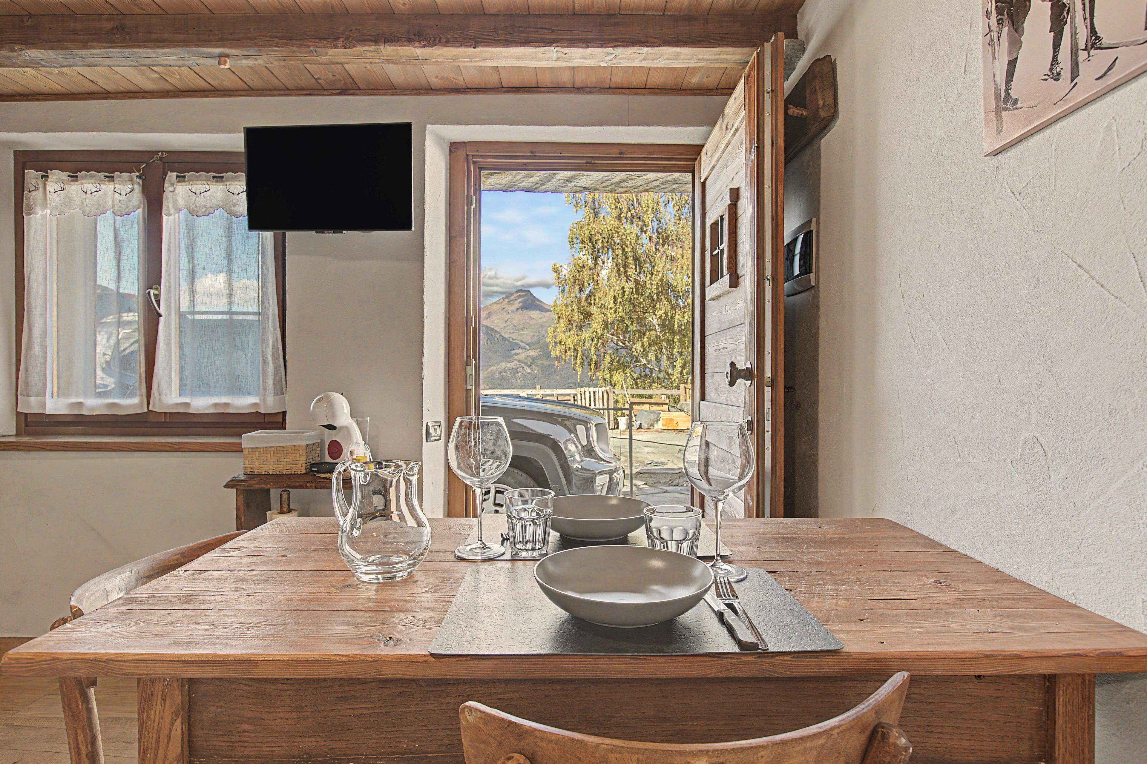 Una mesa de madera para comer con vista a una montaña y un coche afuera.