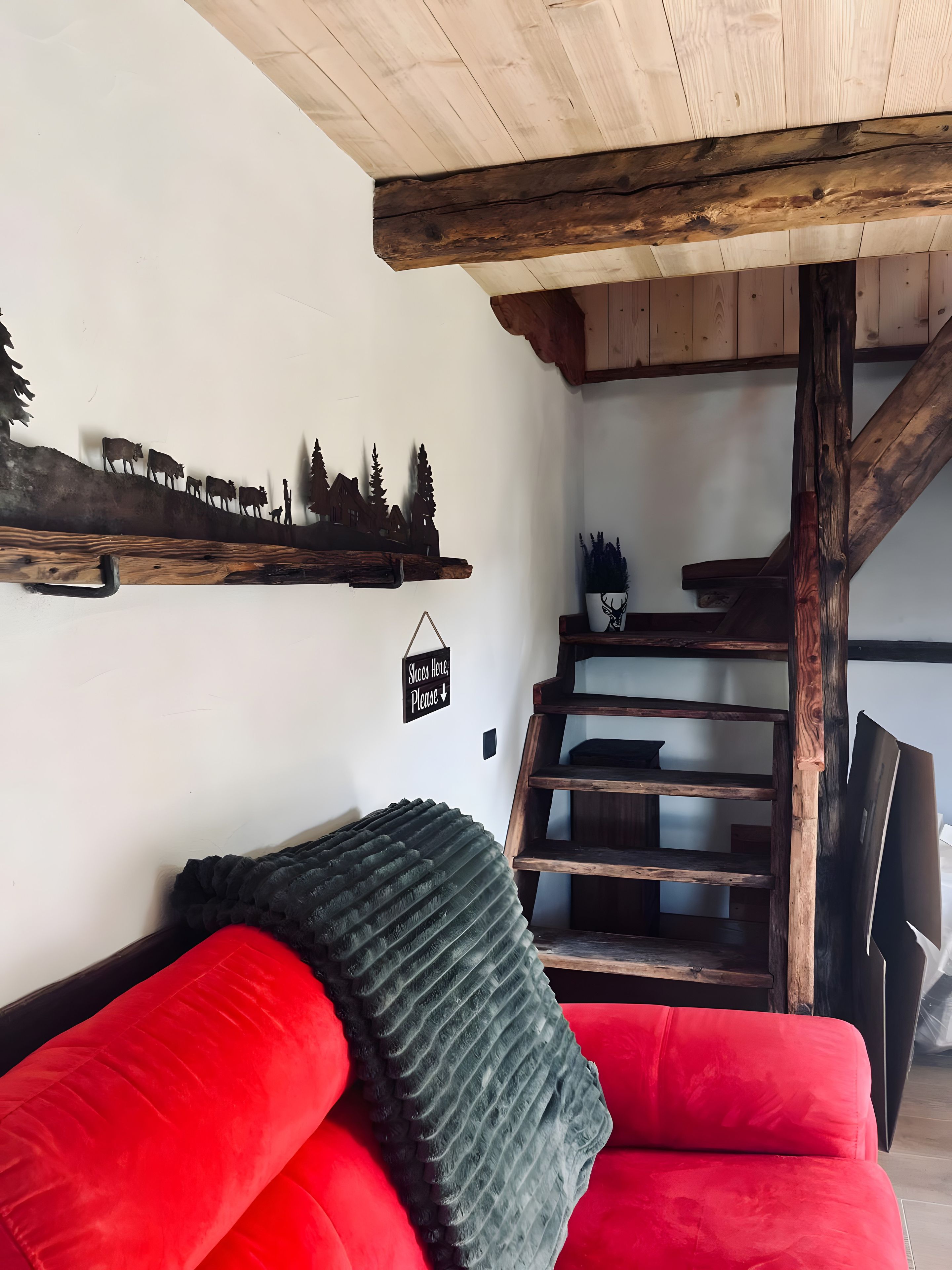 Quarto com sofá vermelho, escada de madeira e prateleira fixada na parede com cena rústica.