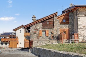 Un edificio tradicional de piedra con contraventanas de madera, un balcón y un muro de piedra.