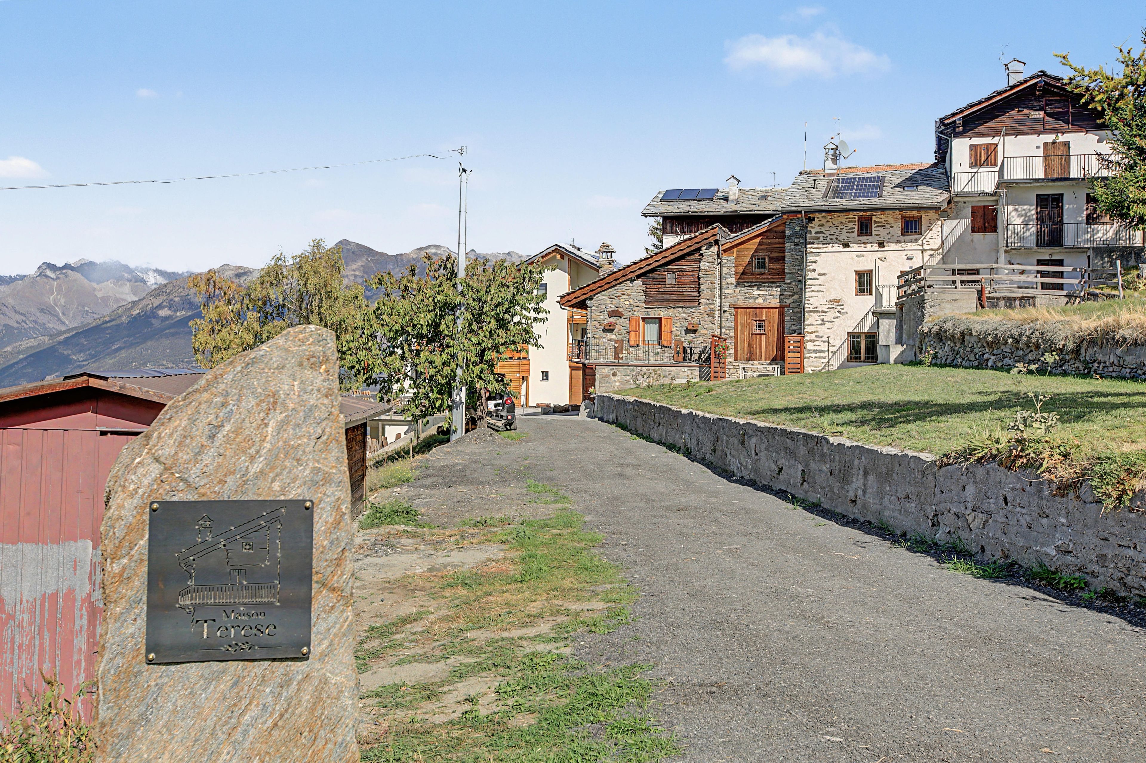 Un sendero de piedra que conduce a edificios tradicionales con montañas al fondo.
