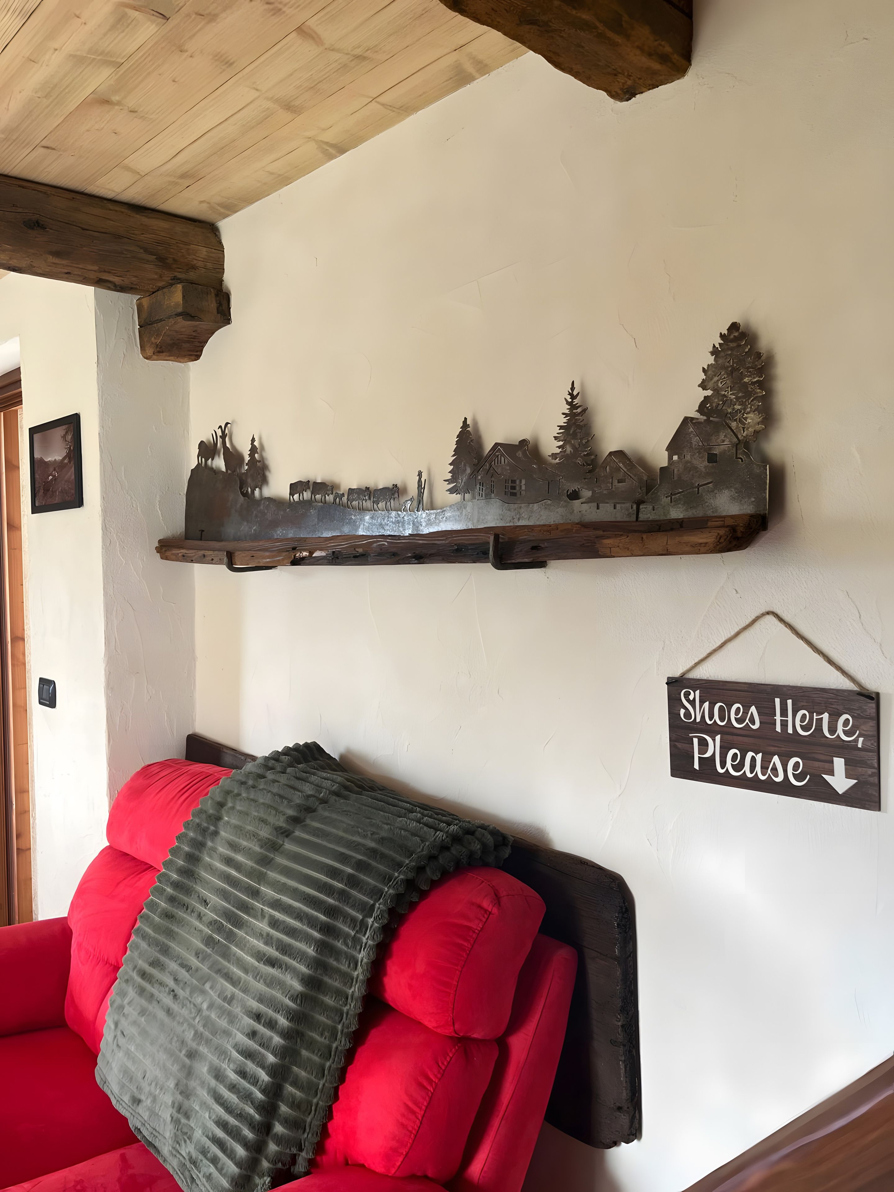 Una sala de estar con un sofá rojo, un adorno metálico en la pared y un letrero que dice 'Shoes Here, Please'.