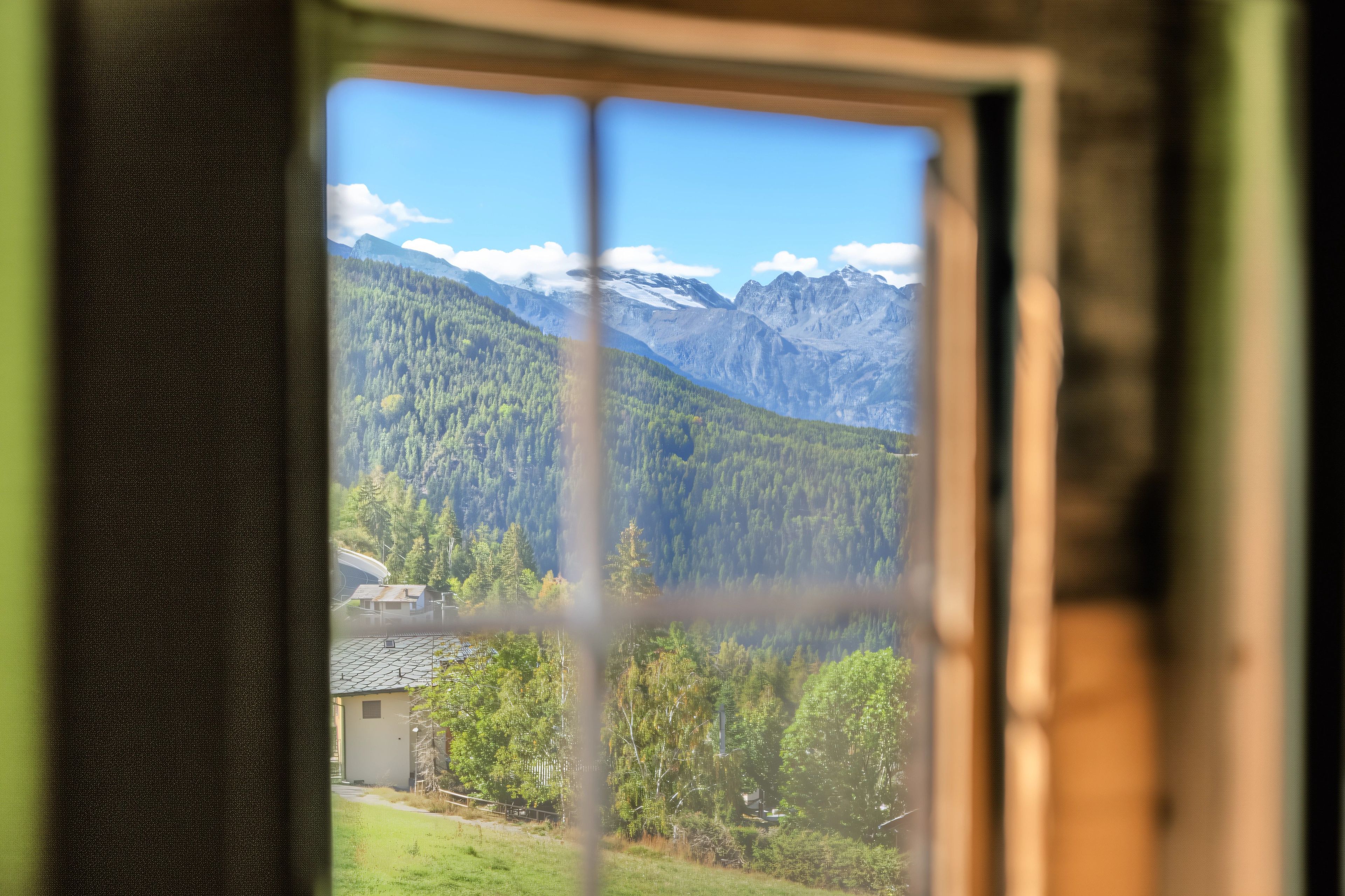 A window with a view of a mountainous landscape, a small building, and a clear sky.