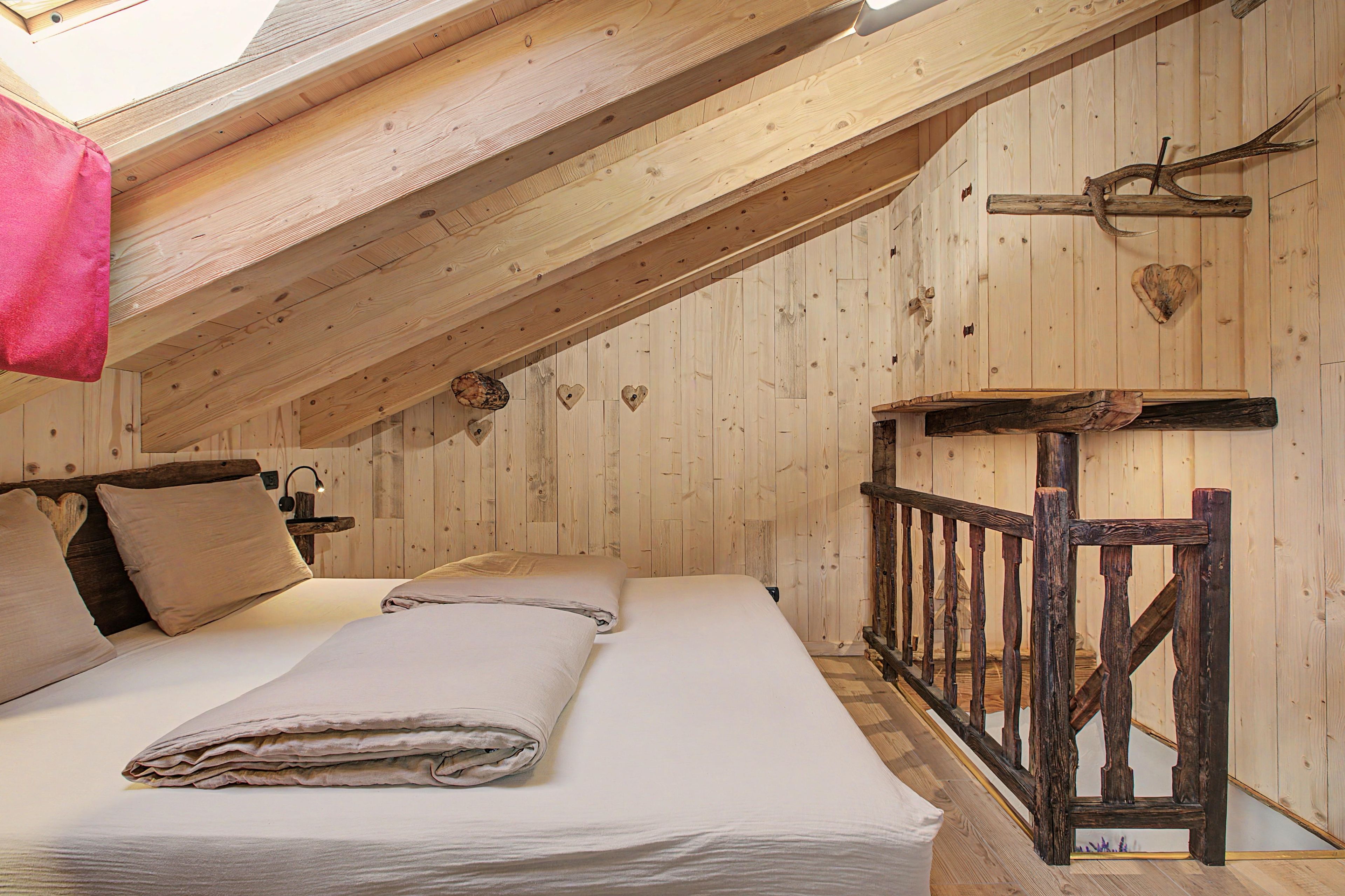 A bedroom with a sloped ceiling, wooden walls, a bed with pillows, a nightstand, and a heart-shaped decoration.