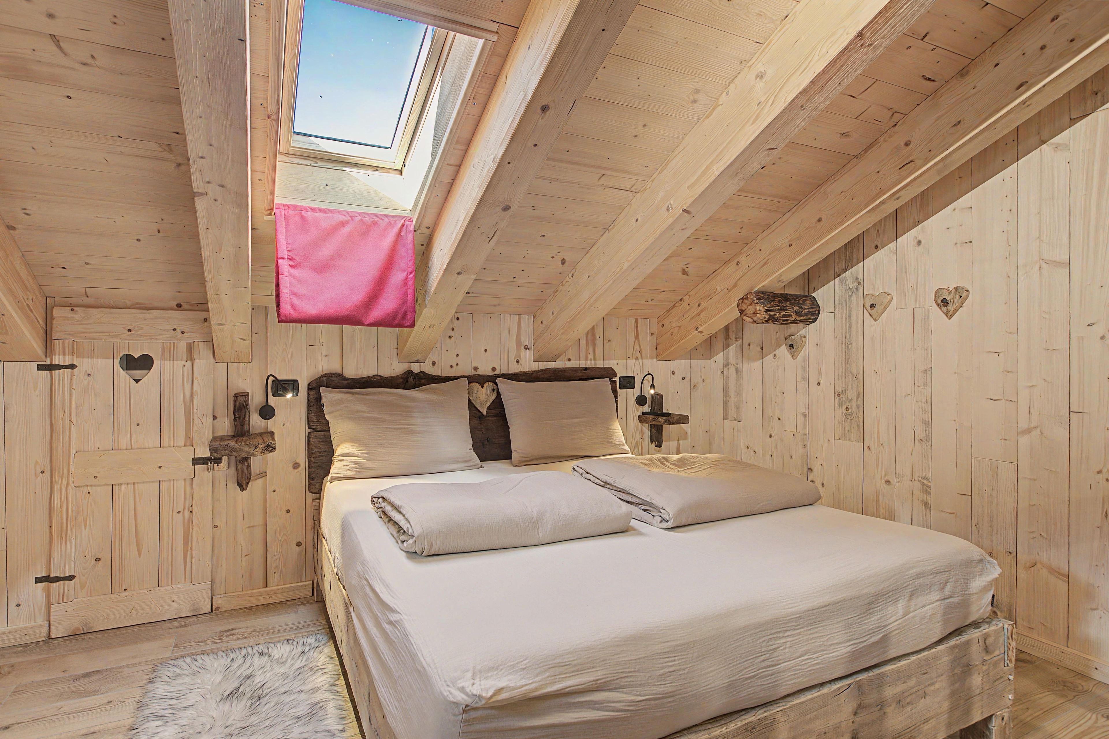 A bedroom with a skylight, wooden walls, a bed with white bedding, and heart-shaped decorations.