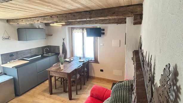 Un interior acogedor con techo de madera, un sofá rojo, una mesa de comedor y una zona de cocina.