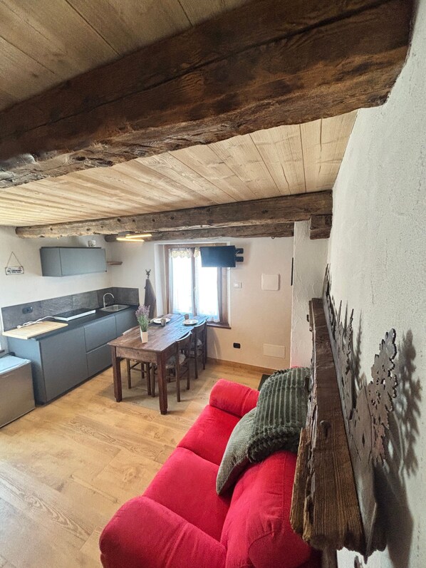 A cozy interior with a wooden ceiling, a red sofa, a dining table, and a kitchen area.