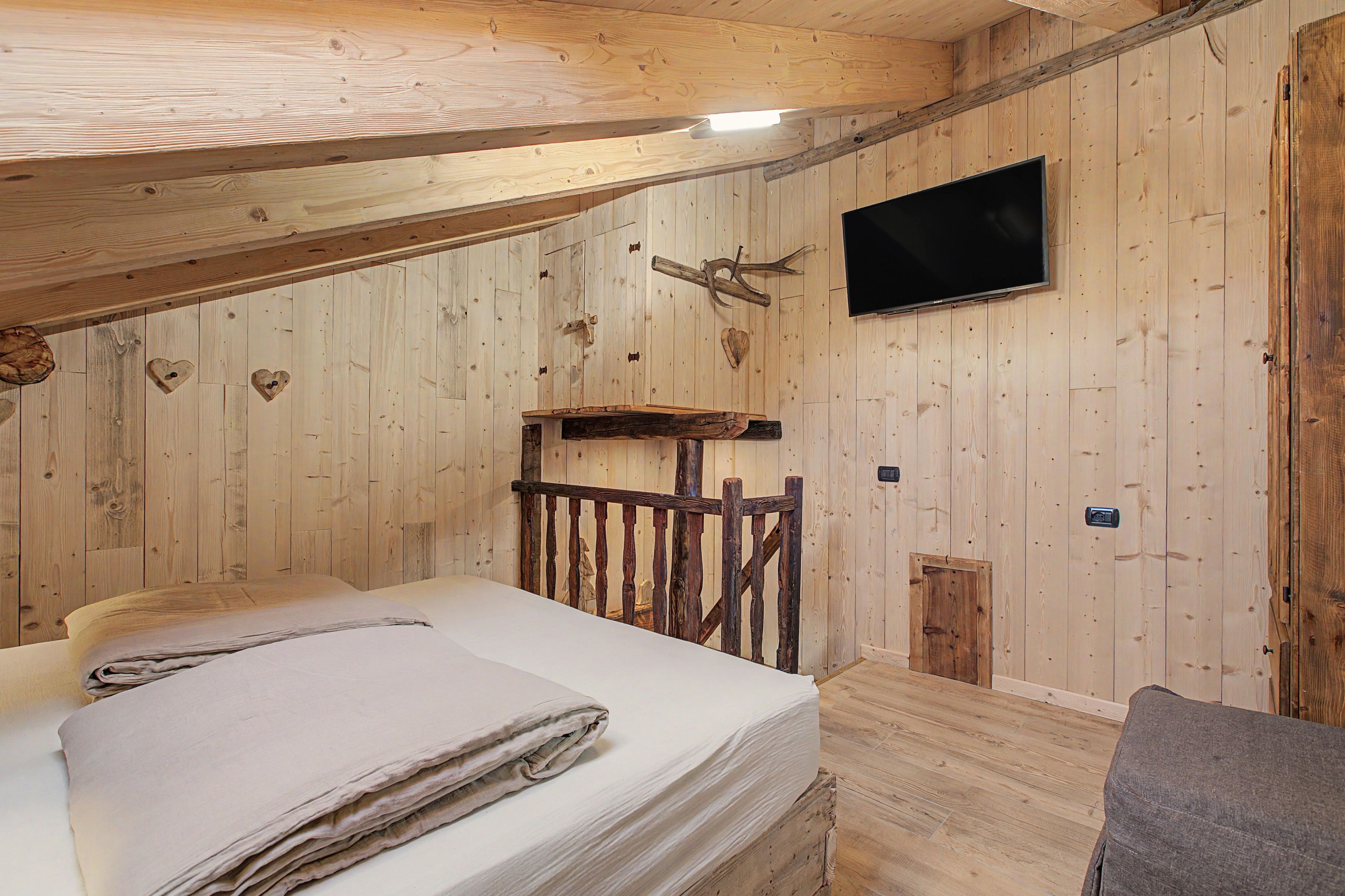 A wooden room with a bed, a mounted television, and a rustic wooden bench.