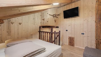 A wooden room with a bed, a mounted television, and a rustic wooden bench.