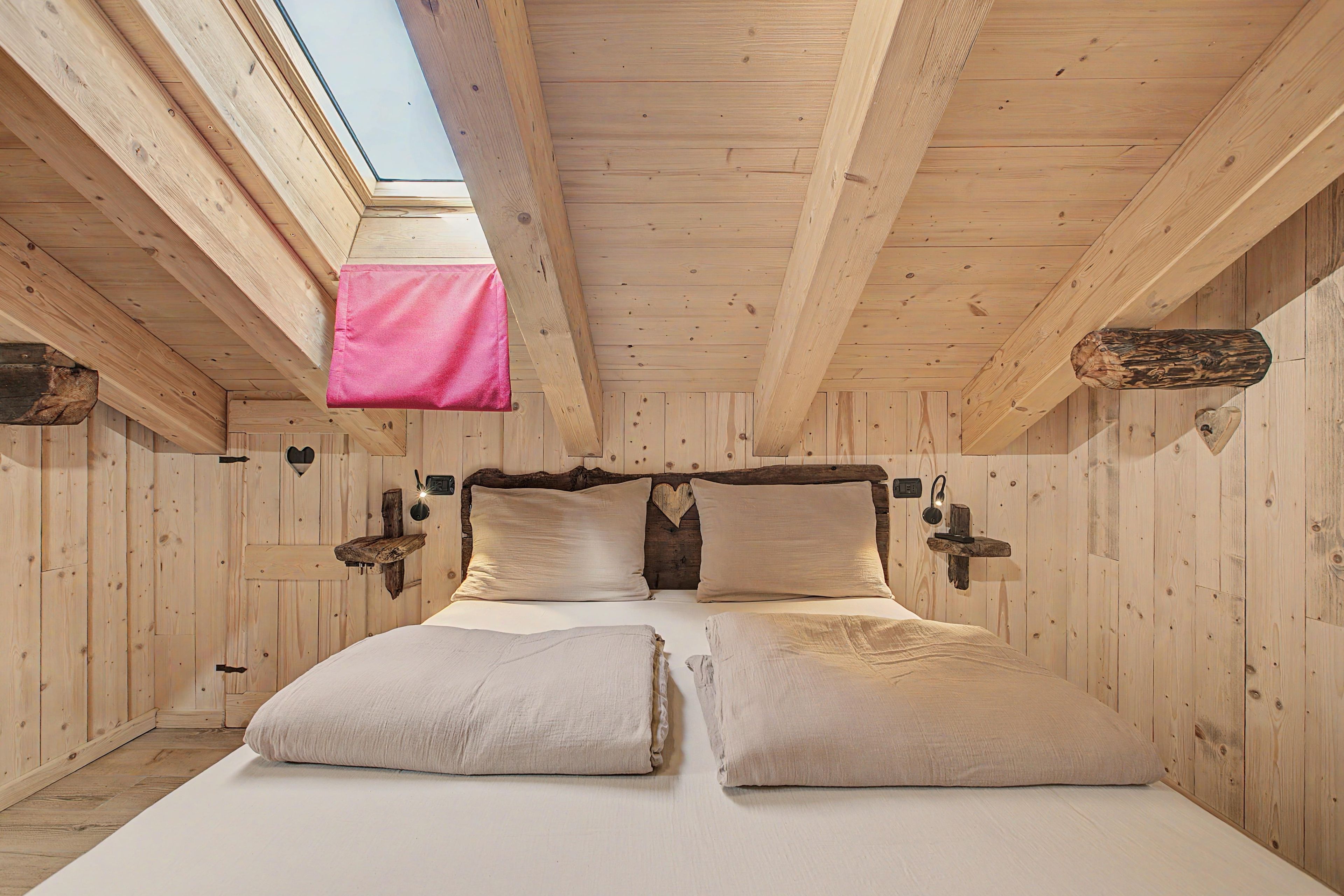 A wooden room with a skylight, a bed with two pillows, and a hanging pink item.