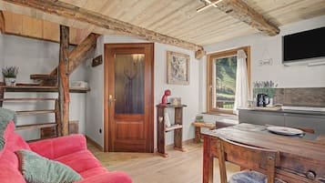 Een rustiek interieur met een houten trap, een rode bank, een eettafel en een keukenhoek.