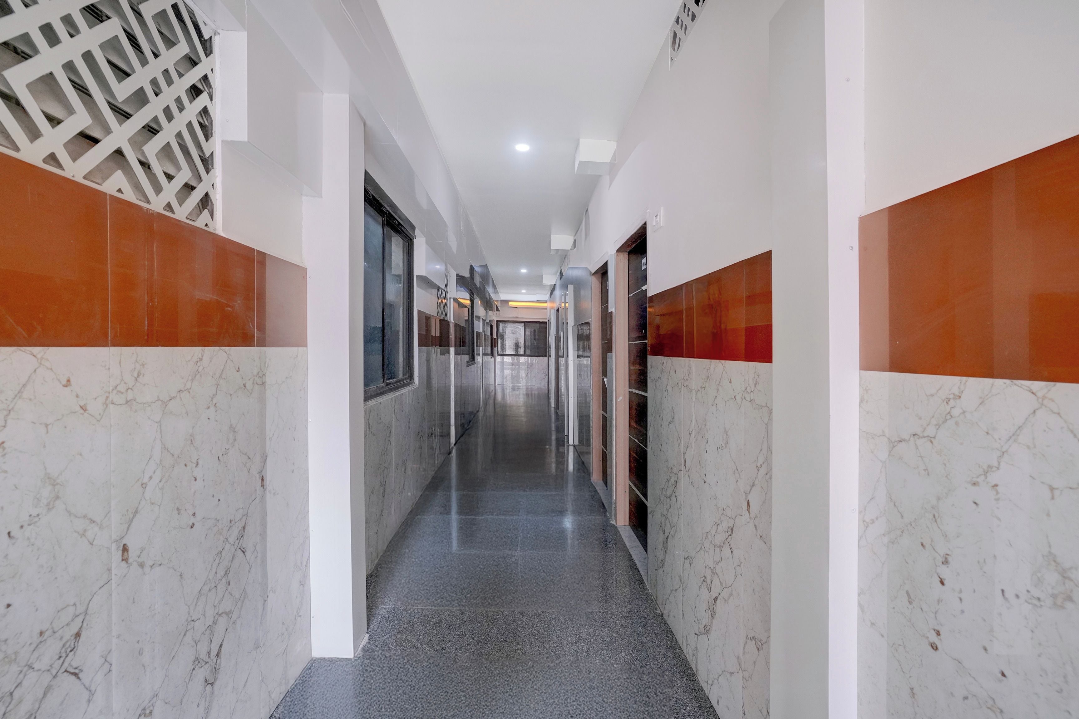 A long, narrow hallway with marble walls and a grey floor, leading to multiple doors.
